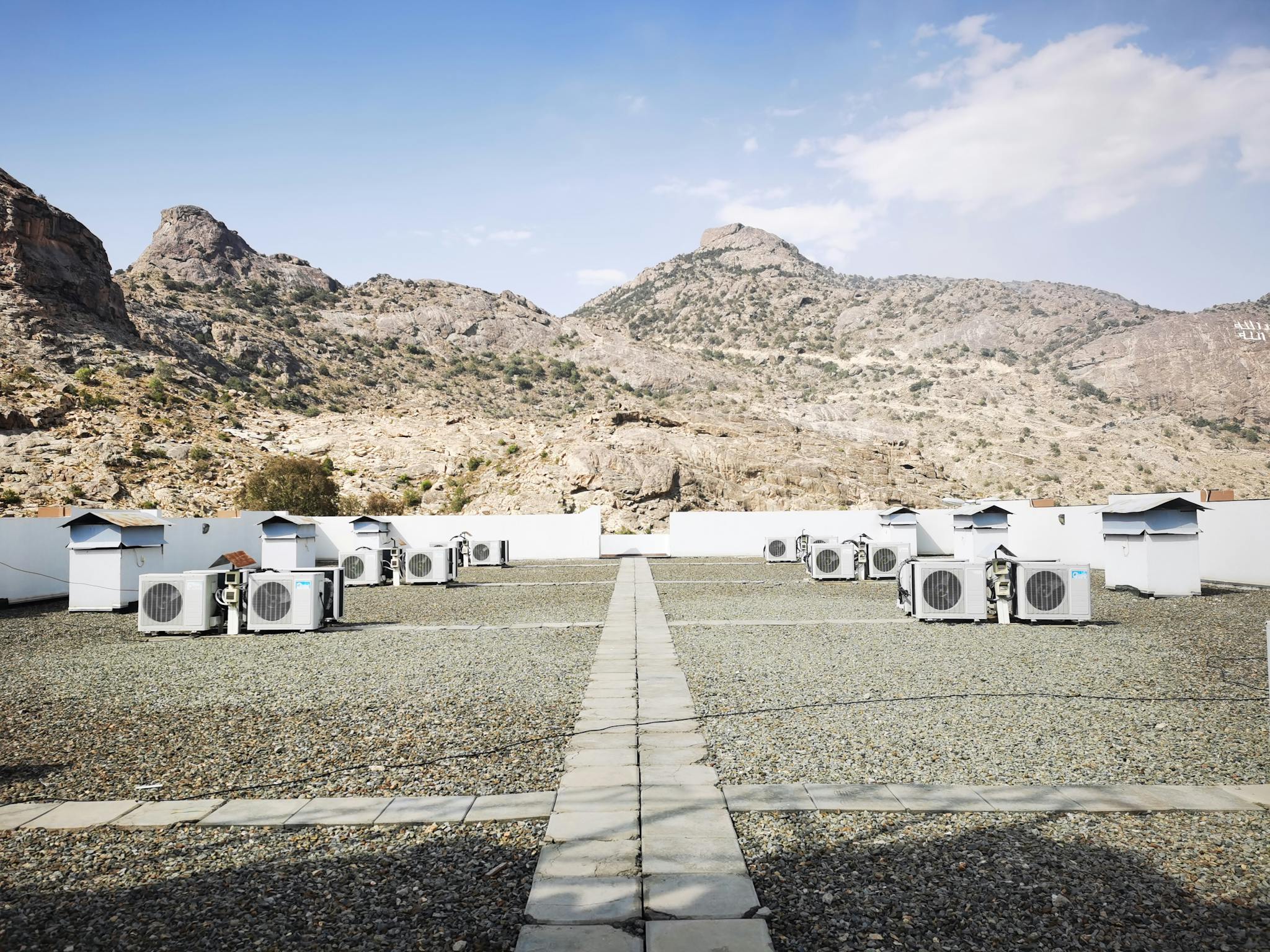 Rooftop air conditioning units on a gravel surface with a mountainous backdrop under a clear sky.